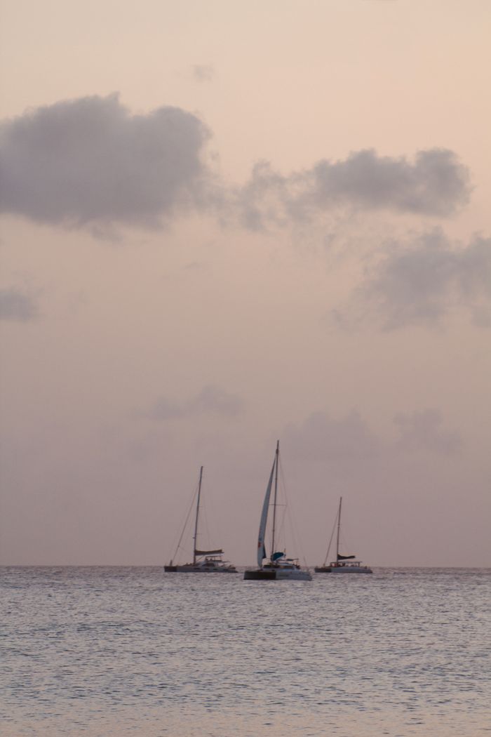 Serene scene of sailboats on calm water during a pastel-hued sunset.